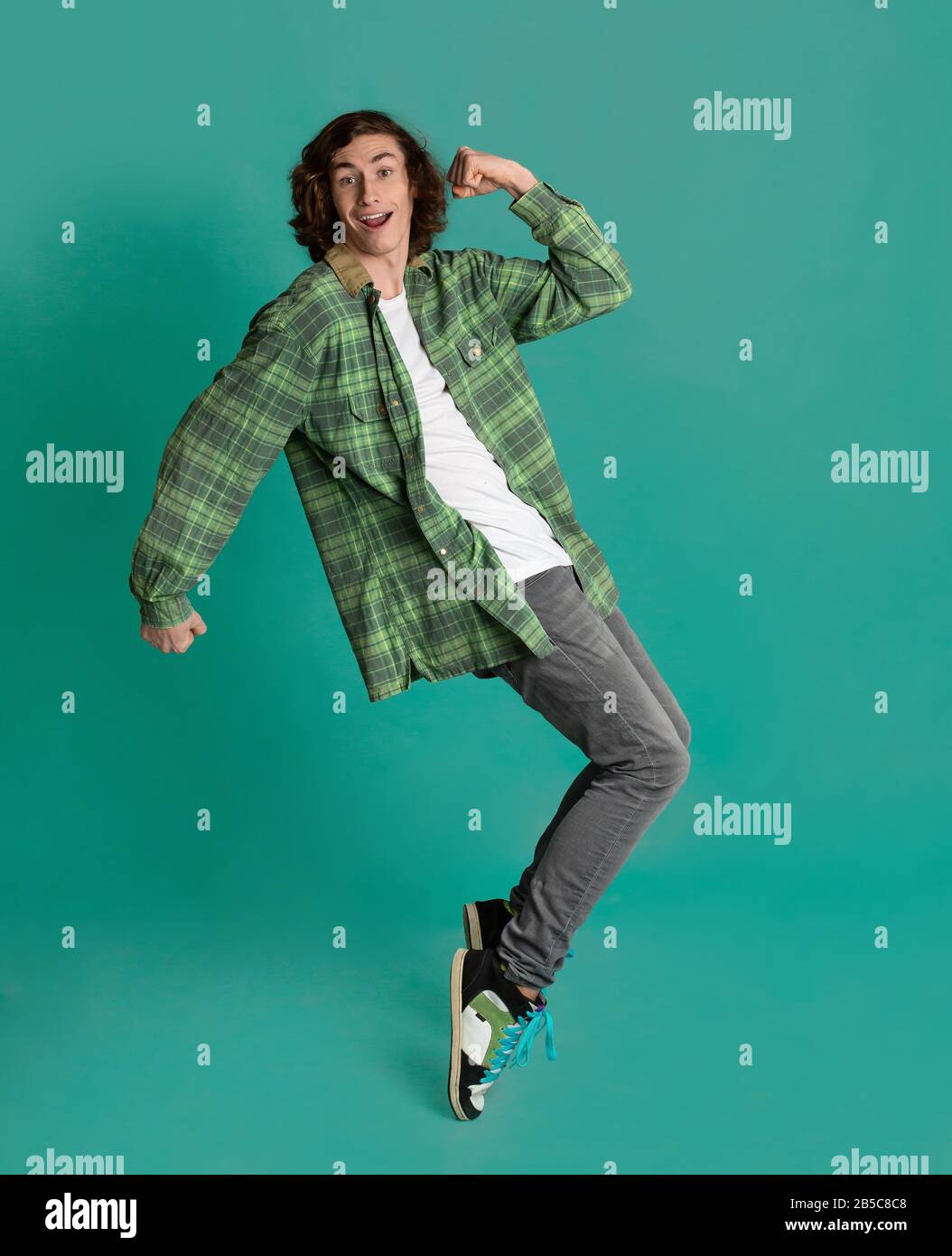 Happy young man standing on tiptoes against turquoise background Stock Photo