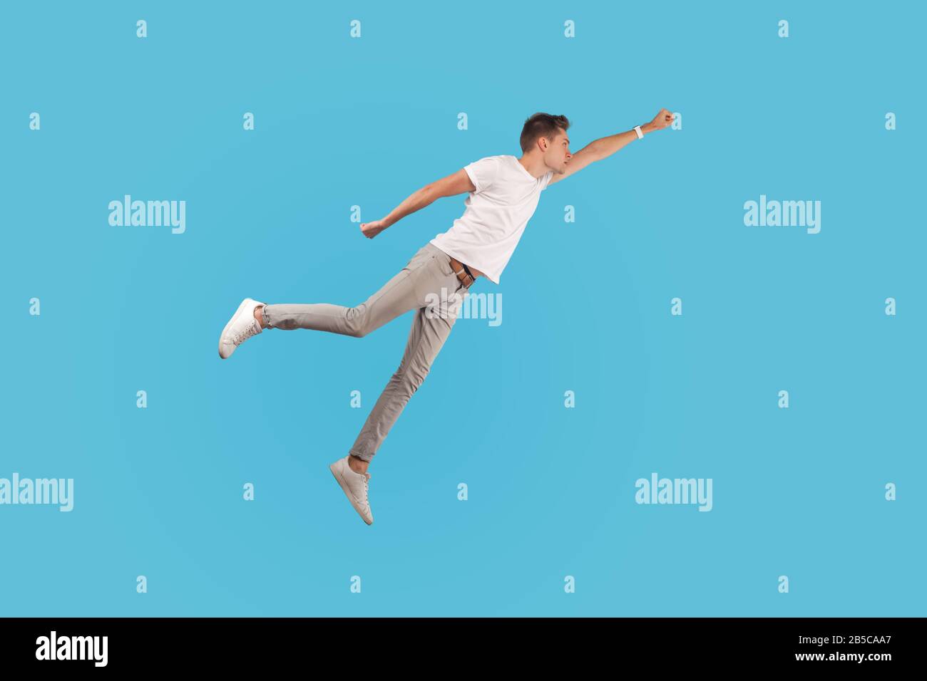 Full length portrait of motivated confident man in white t-shirt and casual pants flying up in air as superhero with raised hand, feeling superpower. Stock Photo