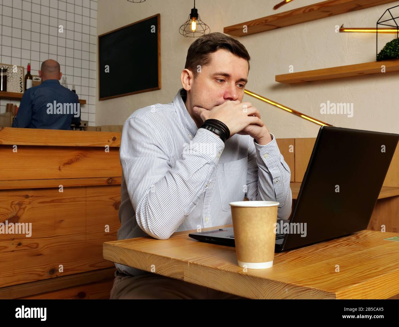 Young man is reading text on laptop and thinking in the cafe. Stock Photo