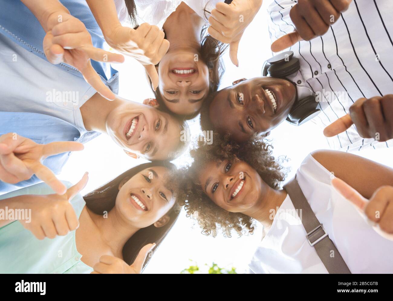 Joyful Multicultural Teenagers Standing In Circle, Showing Funny Gestures, Low Angle Stock Photo