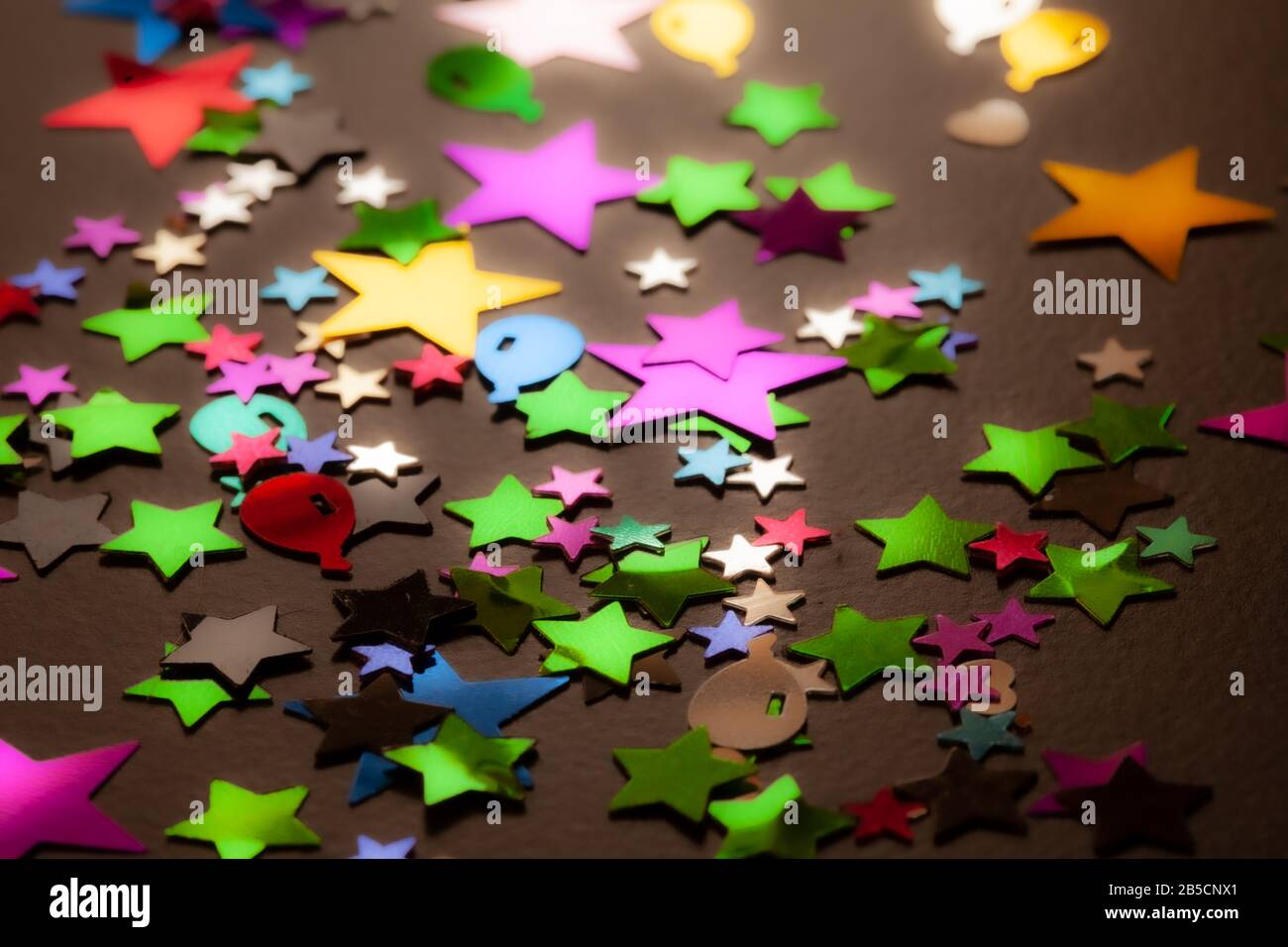 Confetti scattered on a black table background. Stars and other colourful shapes made from multicoloured foil. Stock Photo