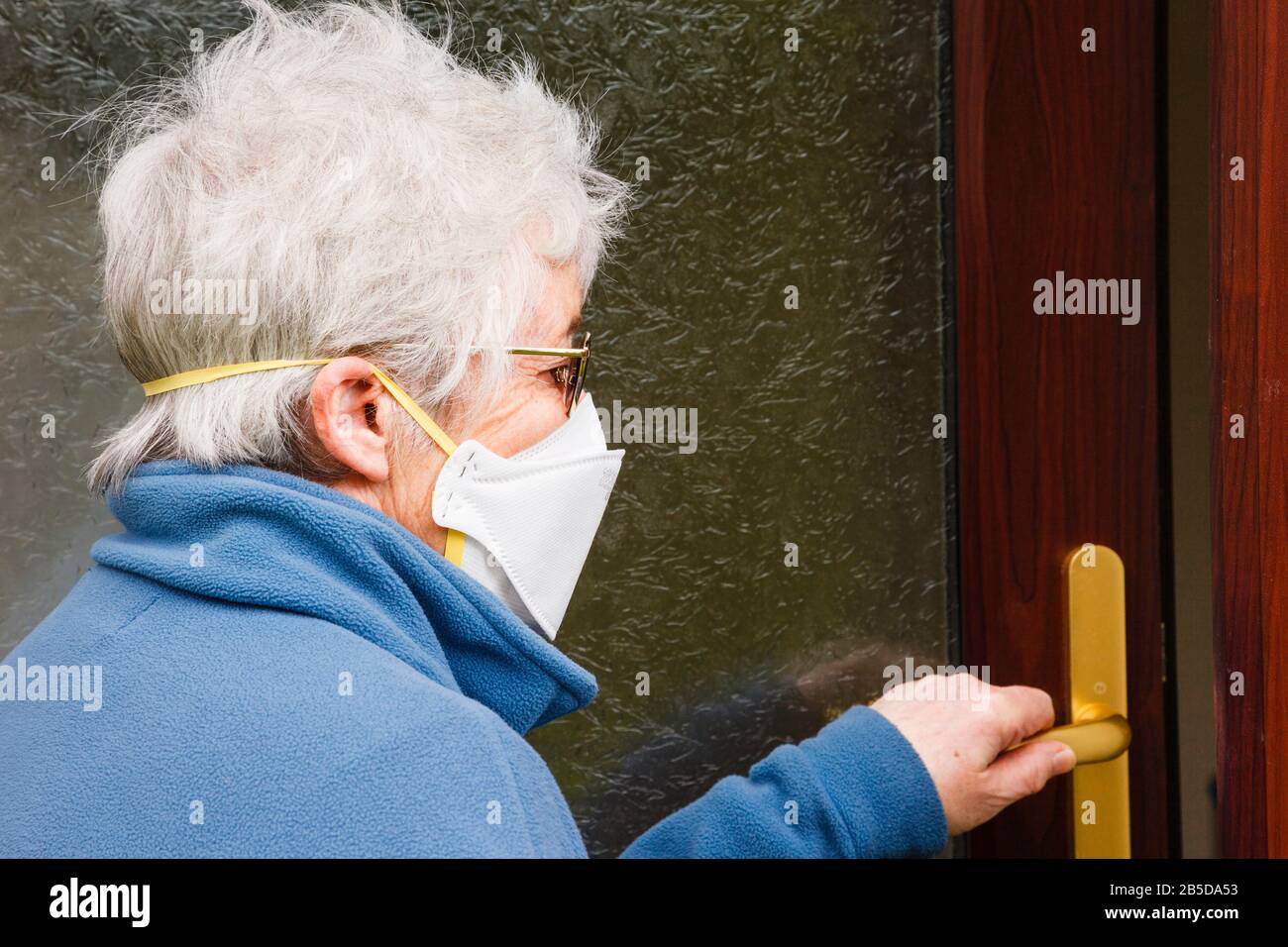 An elderly senior woman going outside wearing a surgical face mask covering nose and mouth to protect against allergens germs and Covid-19 UK Britain Stock Photo