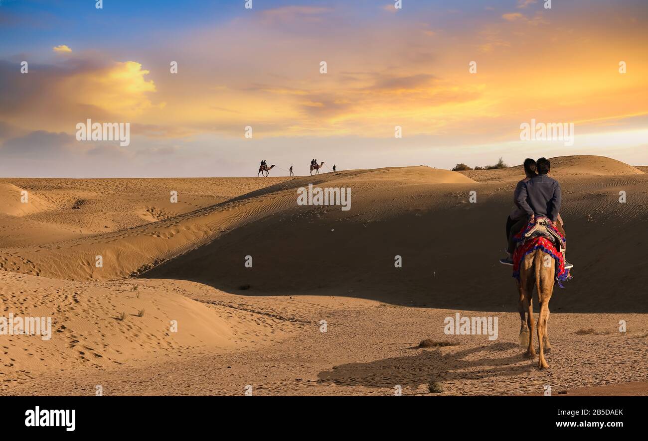 Tourist couple enjoy a camel safari at sunset at the Thar desert Jaisalmer Rajasthan, India Stock Photo