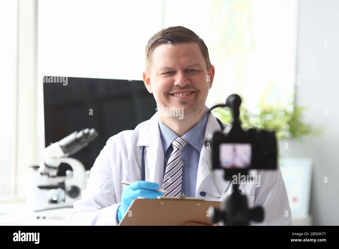 Doctor makes notes in folder in front video camera Stock Photo