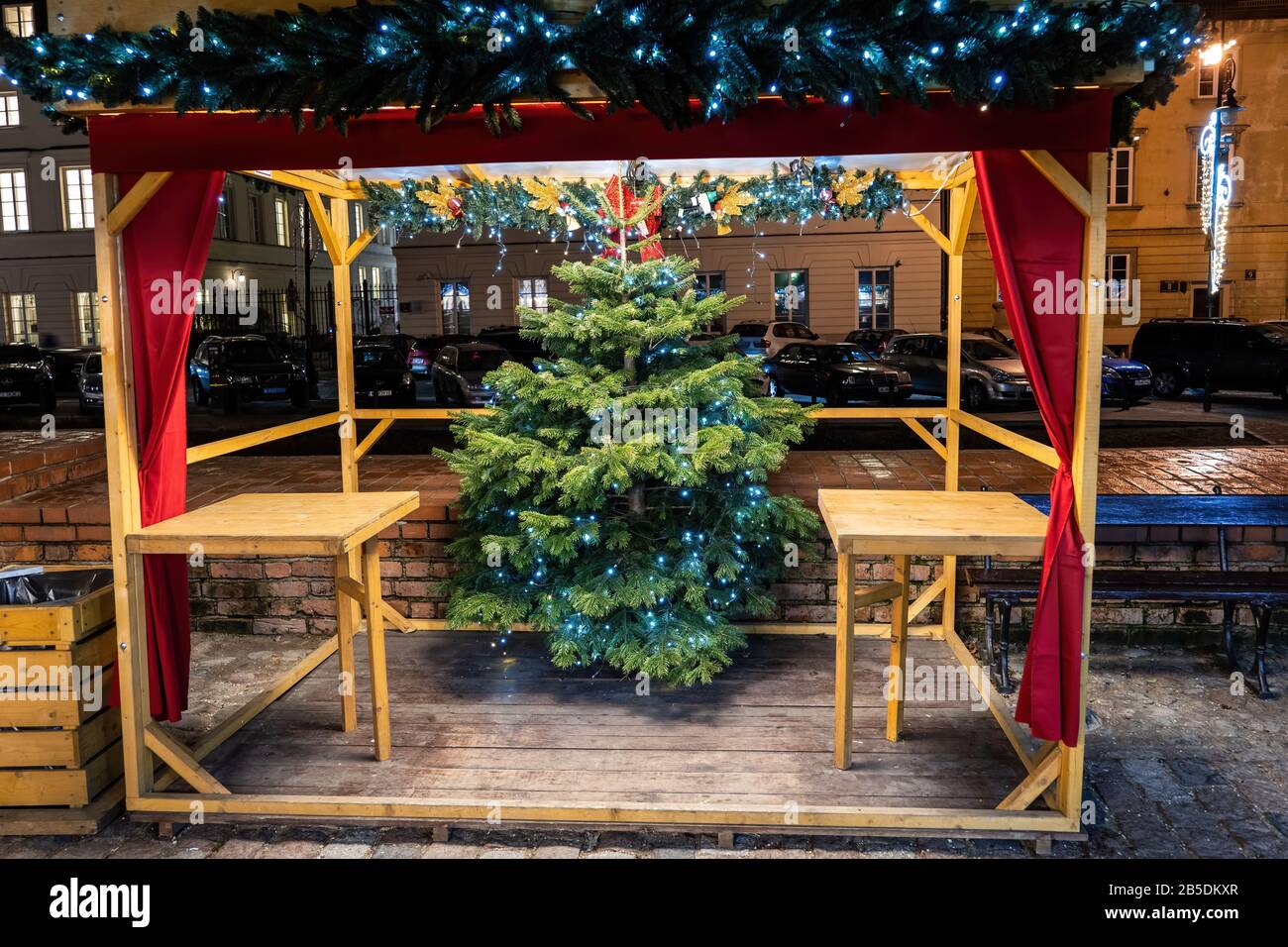 Wooden platform with tables, Christmas tree and decoration next to an alley at holiday market, free roofed space ready for people to enjoy their snack Stock Photo