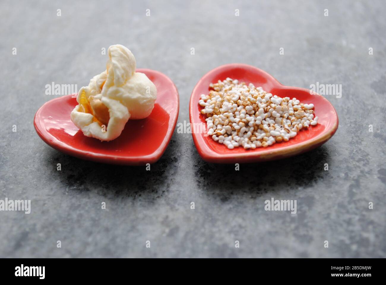 One popcorn and many small popped amaranth seeds on heartshaped little dollhouse plates. Stock Photo