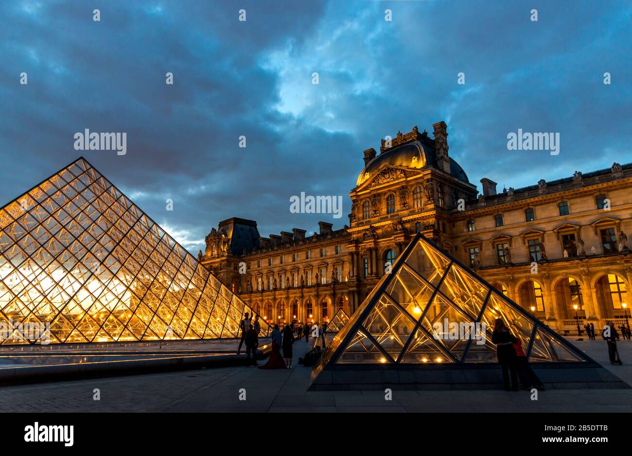 Evening view of the Louvre Museum with the pyramids lit and a dramatic sky in Paris, France. Stock Photo