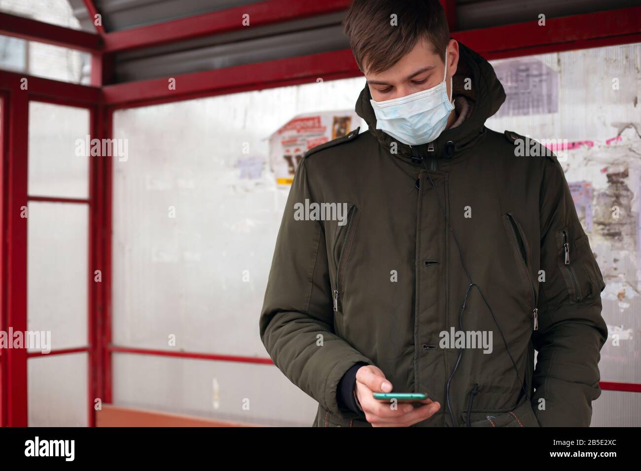 guy in a medical mask stands at a bus stop. isolated to avoid viral disease covid-19 measles flu chickenpox cold. Stock Photo