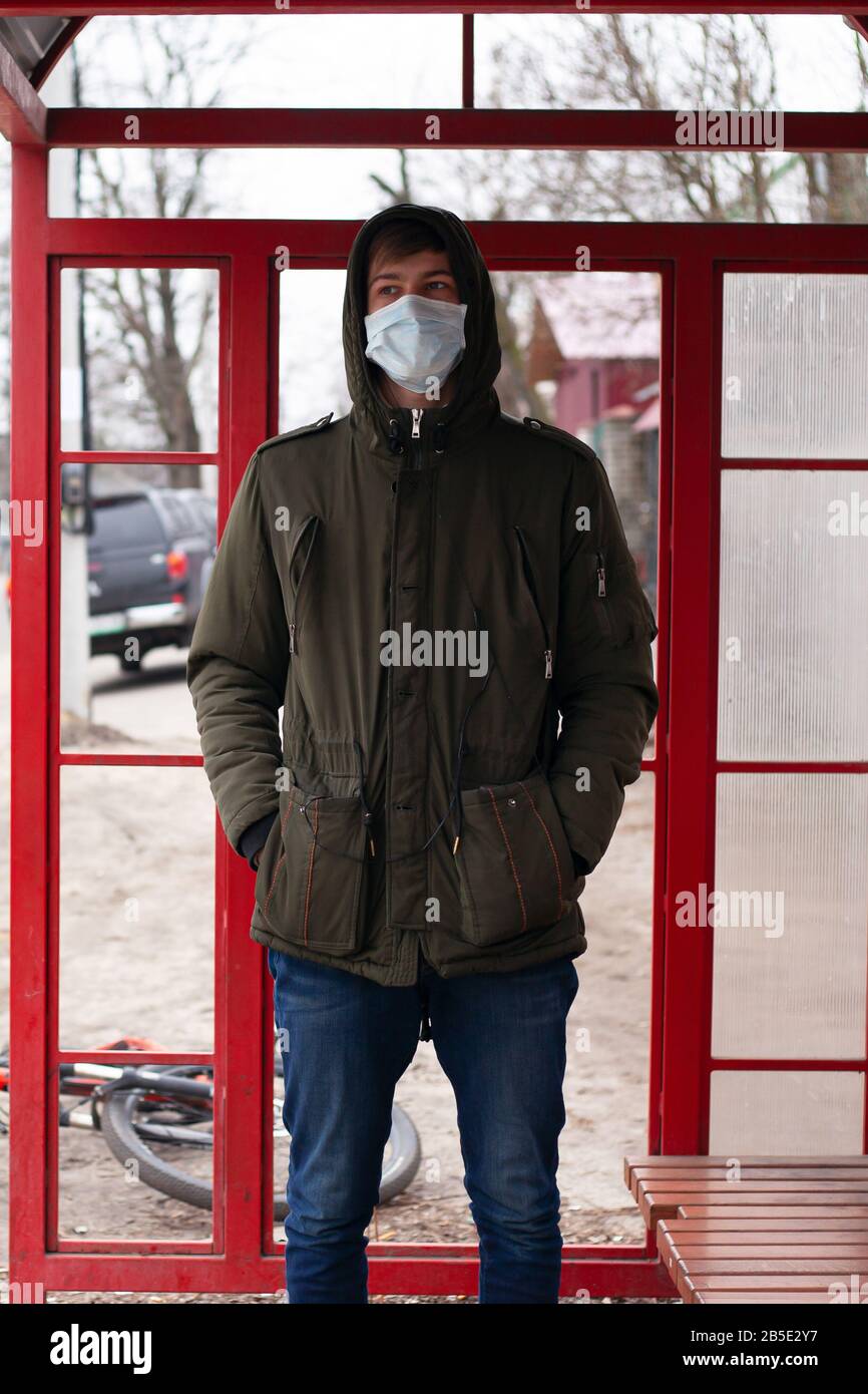 guy stands at a bus stop in a medical disposable mask. respiratory viral disease protection covid-19 flu measles cold. Stock Photo