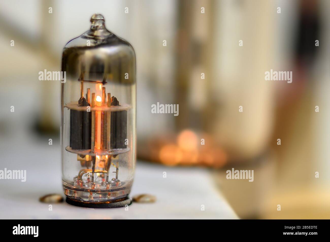 A single glowing vacuum tube. Other tube blowing in the background but outside the shallow depth of field. Stock Photo