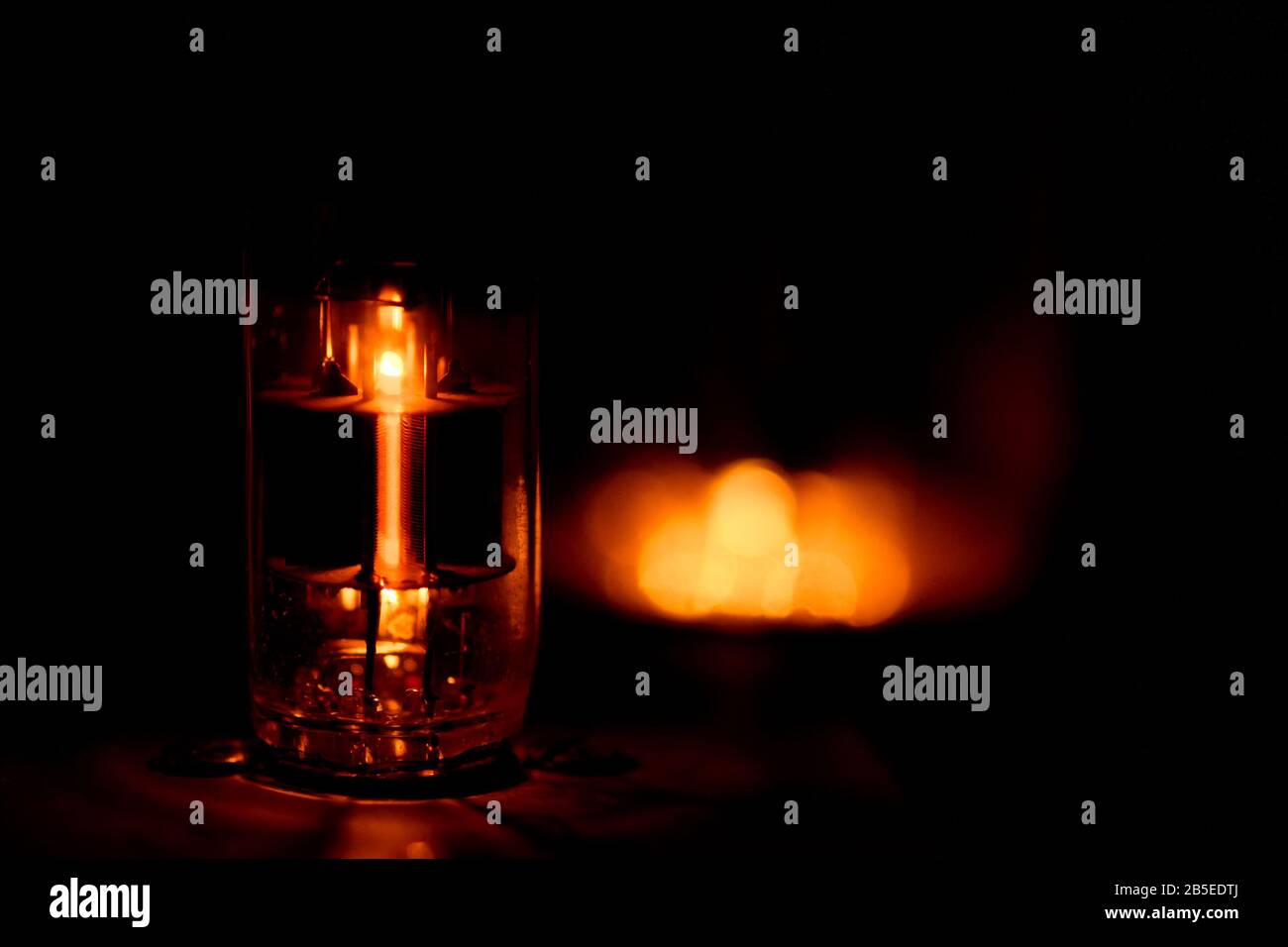 A single glowing vacuum tube in the dark. Other tube blowing in the background but outside the shallow depth of field. Stock Photo