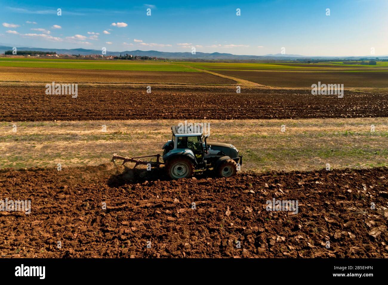 Aerial drone shot of a farmer in tractor seeding, sowing agricultural crops at field in the fertile farm fields of Kilkis in North Greece Stock Photo