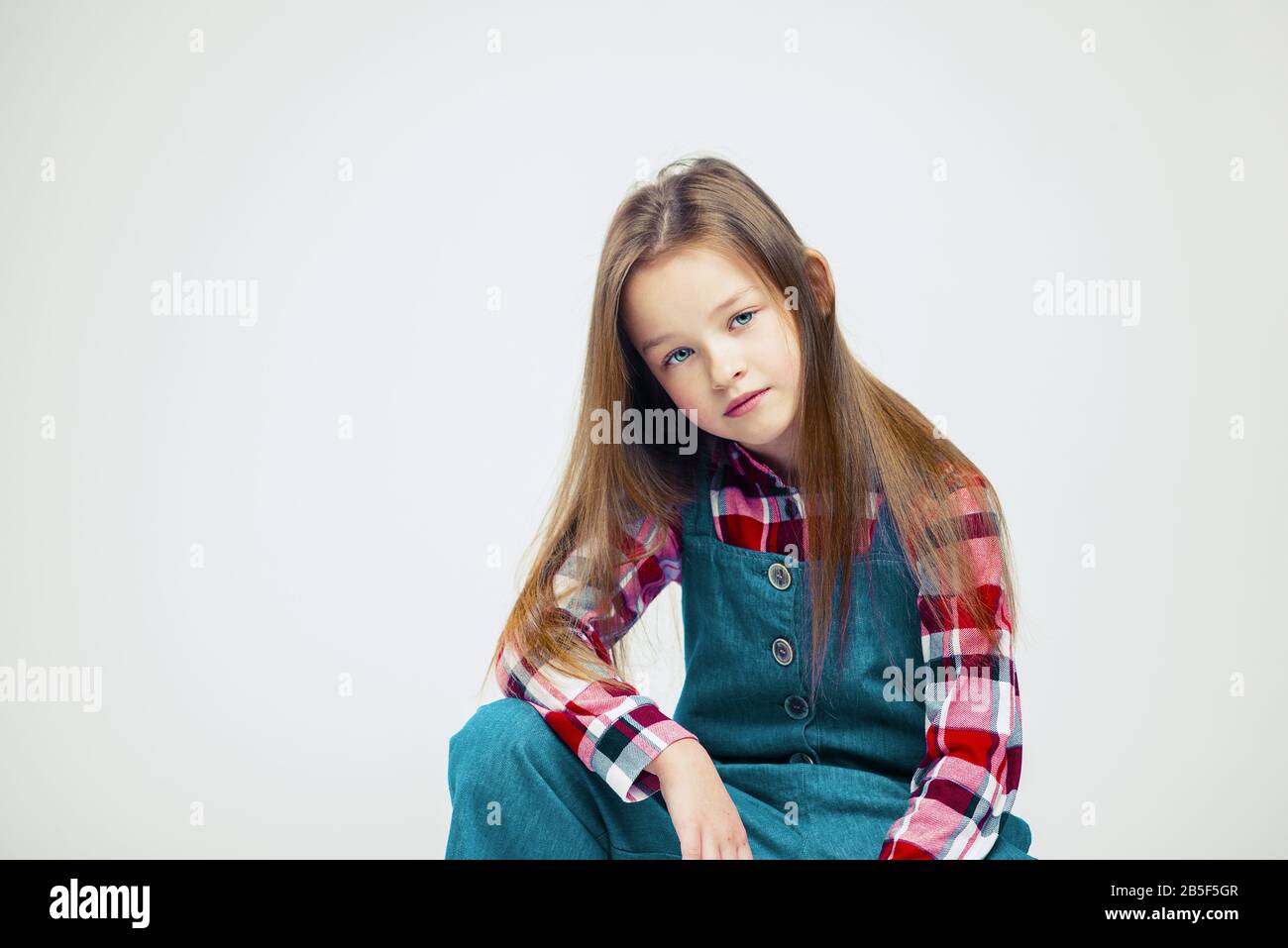 Portrait of a pretty little girl in jeans and a plaid shirt. studio ...