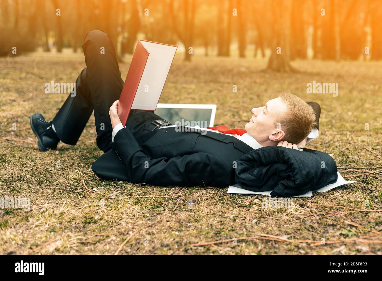 young guy lying in nature with laptop. businessman working remotely outdoors. freelancer reads documents. toned Stock Photo