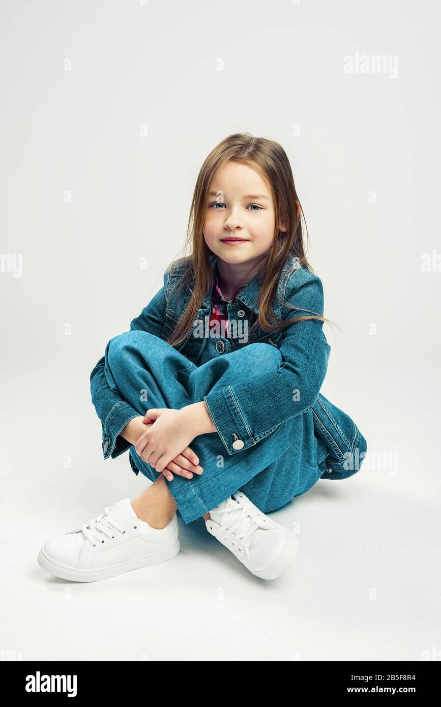 Studio portrait of a cute little girl. kids fashion child in denim pants  and jacket and white sneakers. gray background Stock Photo - Alamy