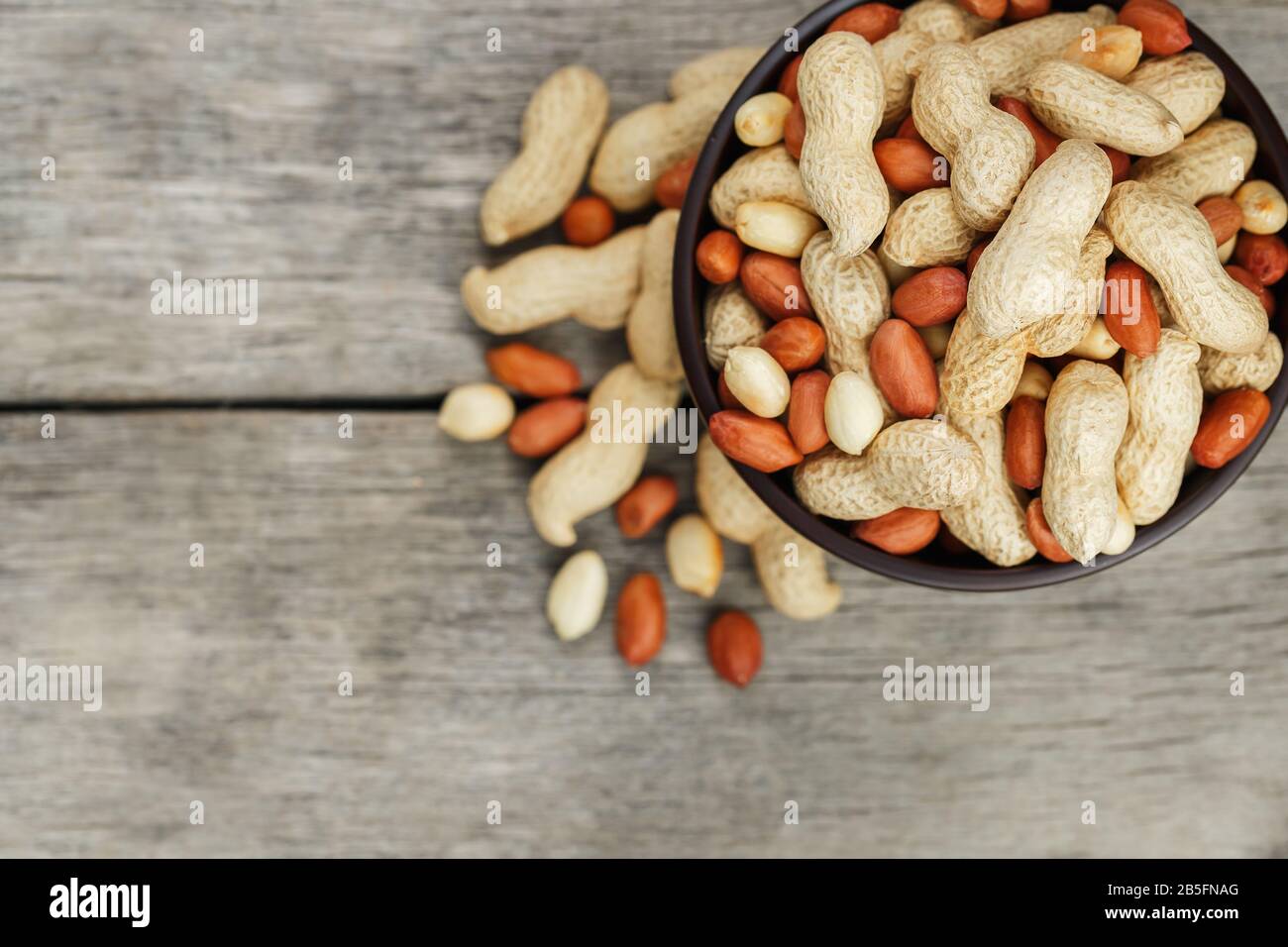Roasted peanuts in their shells and peeled in a brown cup, against a gray wooden table. Organic vegetarian protein, macro. Stock Photo