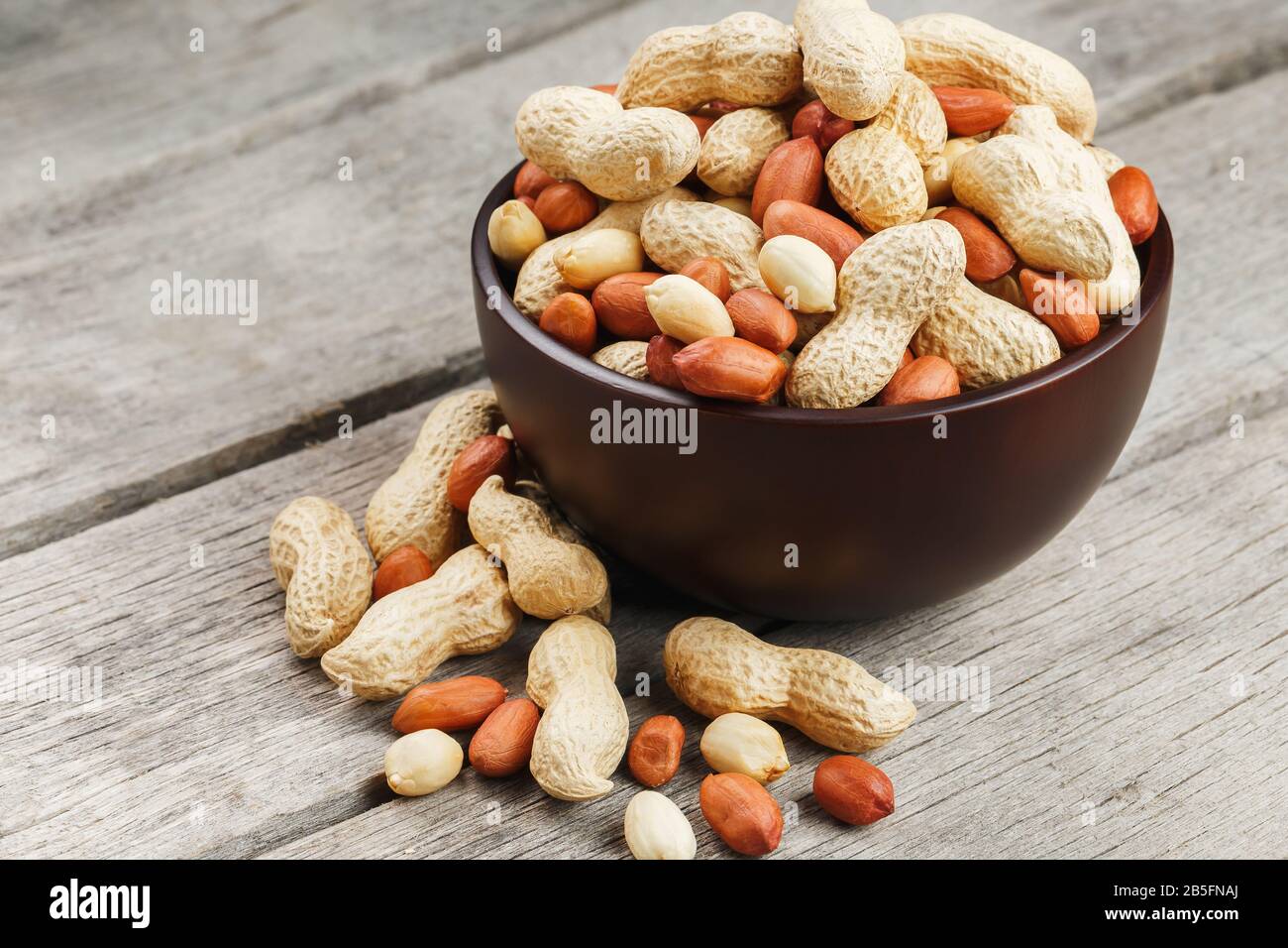 Roasted peanuts in their shells and peeled in a brown cup, against a gray wooden table. Organic vegetarian protein, macro. Stock Photo