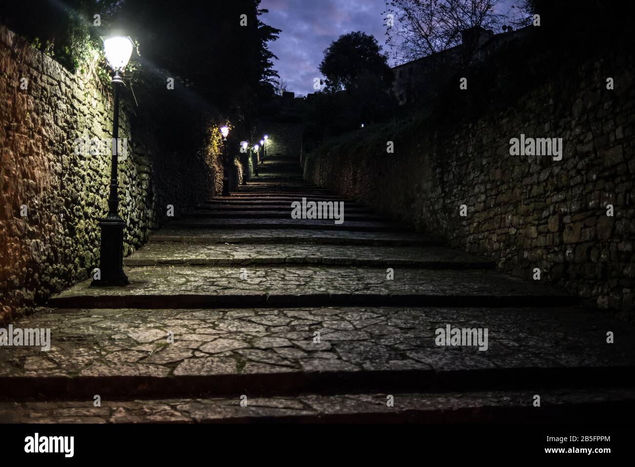 Dark medieval cobbled alley at night with several street lamps providing light Stock Photo