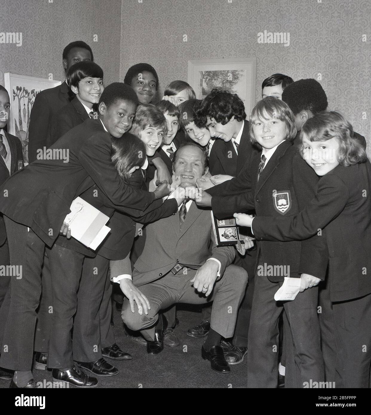 1972, historical, 'take it on the chin'....British boxing legend Henry Cooper having fun with a group of uniformed schoolboys on a visit to an inner city secondary school in South London, England, UK. Stock Photo