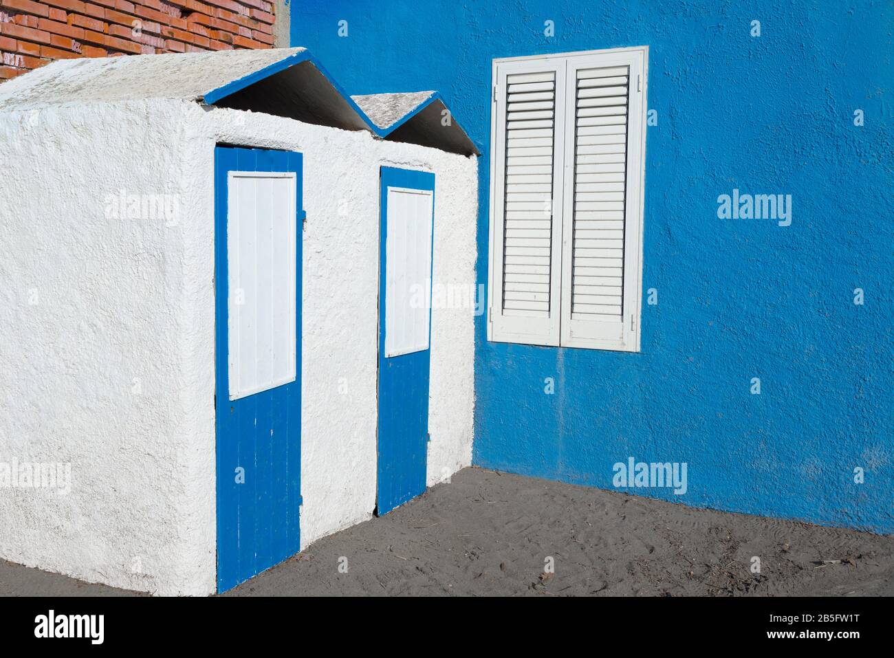 Seaside cabins in concrete painted in pastel blue and white next to blue wall with white window with closed shutters Stock Photo
