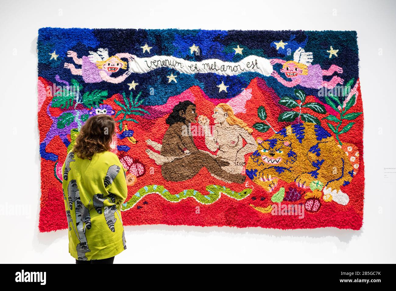 Brown-haired woman looking at 'Love is both Honey and Venom', rug artwork by Anna-Karoliina Vainio, at Amos Rex art museum in Helsinki, Finland Stock Photo