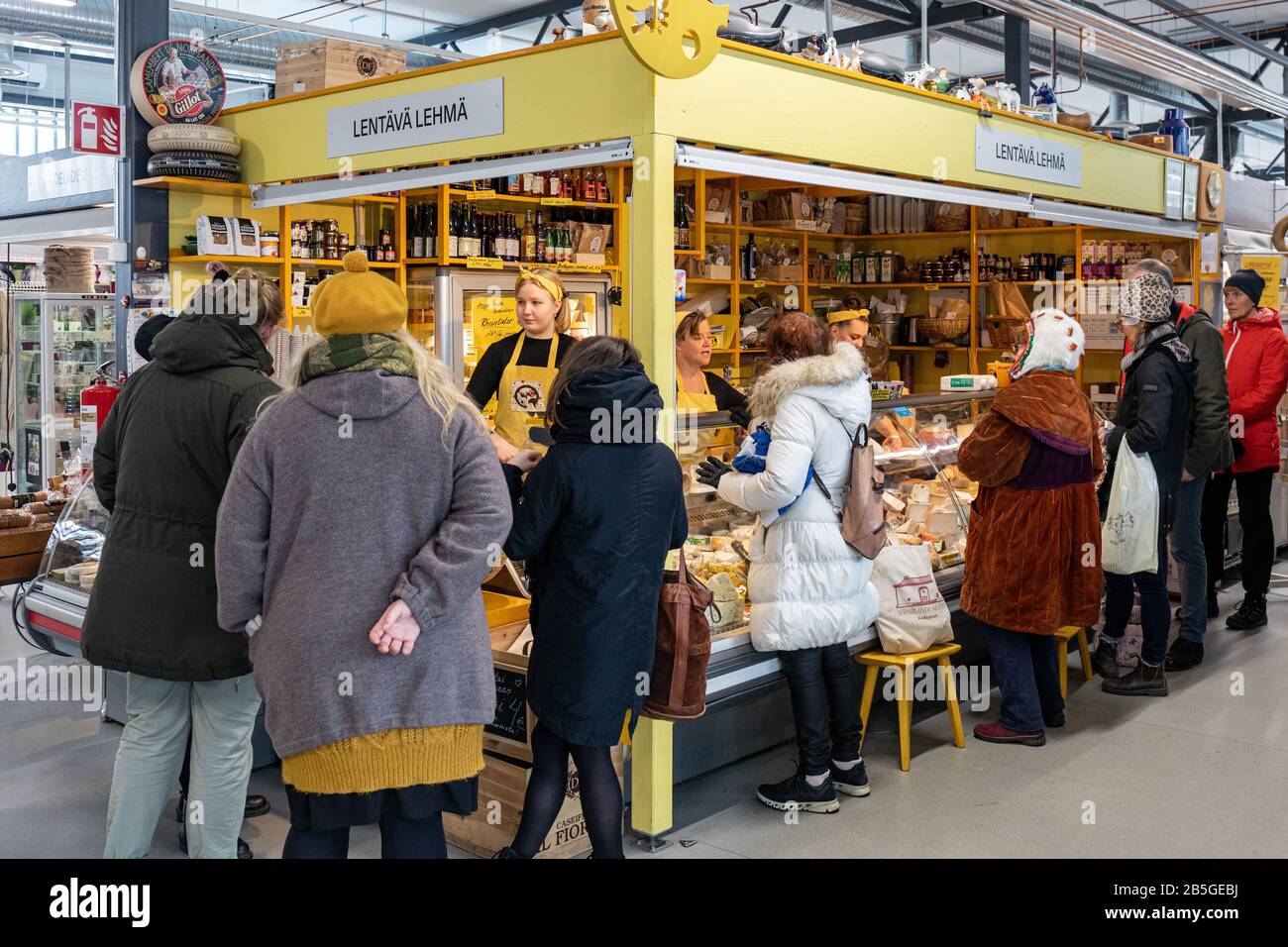 Customers in front of Lentävä Lehmä, yellow cheese vendor stall at Hakaniemi temporary indoor market hall in Helsinki, Finland Stock Photo