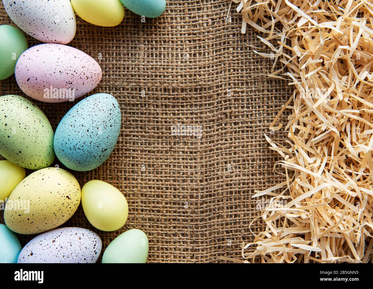 Easter eggs on a sackcloth and straw . Happy Easter multicolored easter eggs. Background with easter eggs. Flat lay, top view. Stock Photo