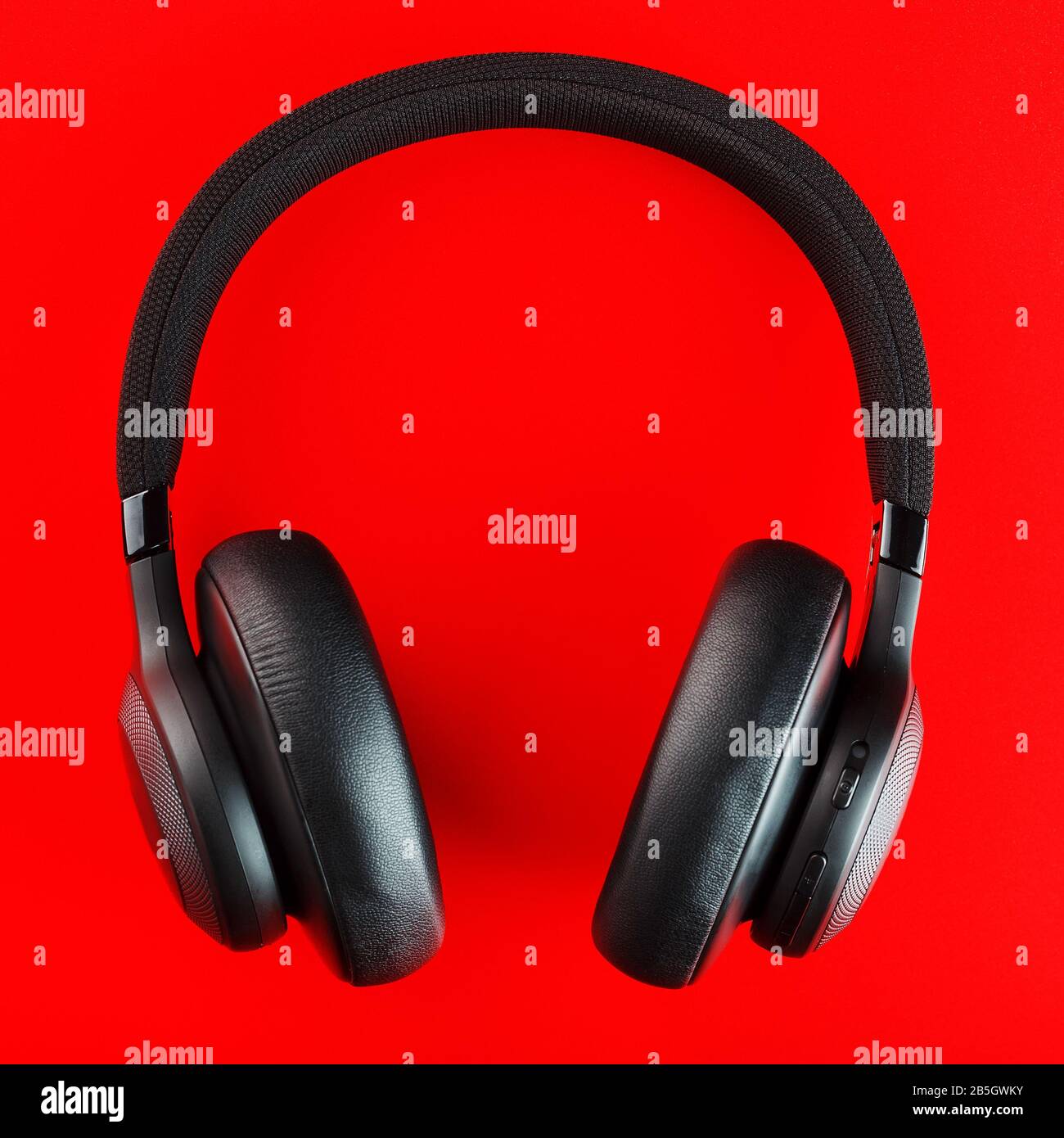 Black wireless headphones on a red background. Overhead, isolated