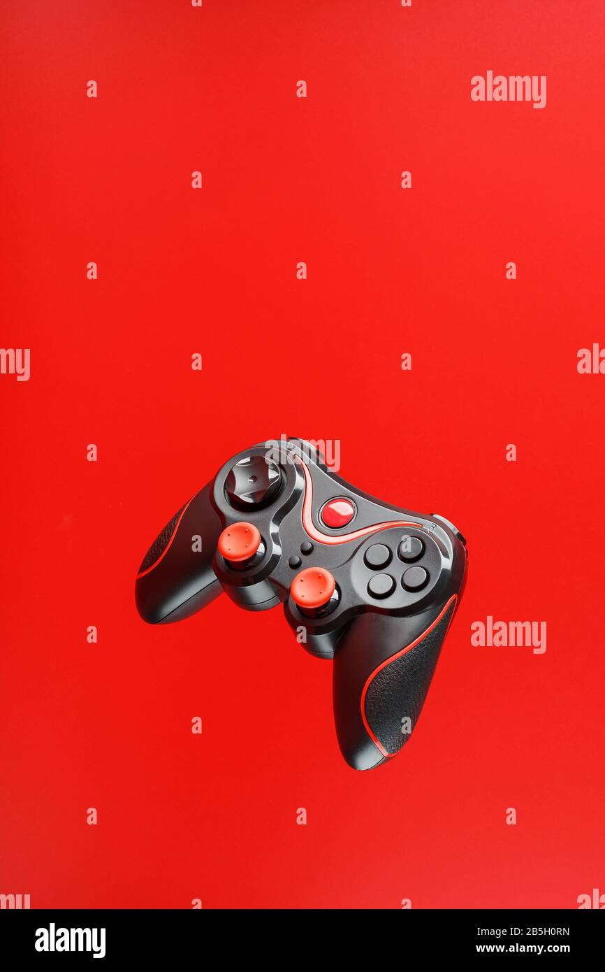 A black joystick game controller hovers isolated on a red background ...