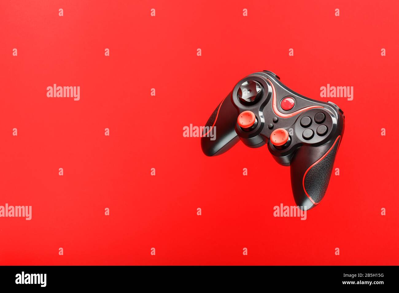 A black joystick game controller hovers isolated on a red background ...