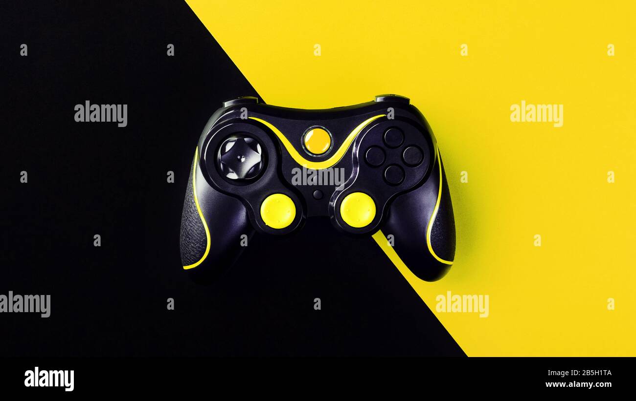 Black gamepad on a black-yellow background, G. Game concept. Device to control and control the game. Video games on PC, console, smartphone. Stock Photo