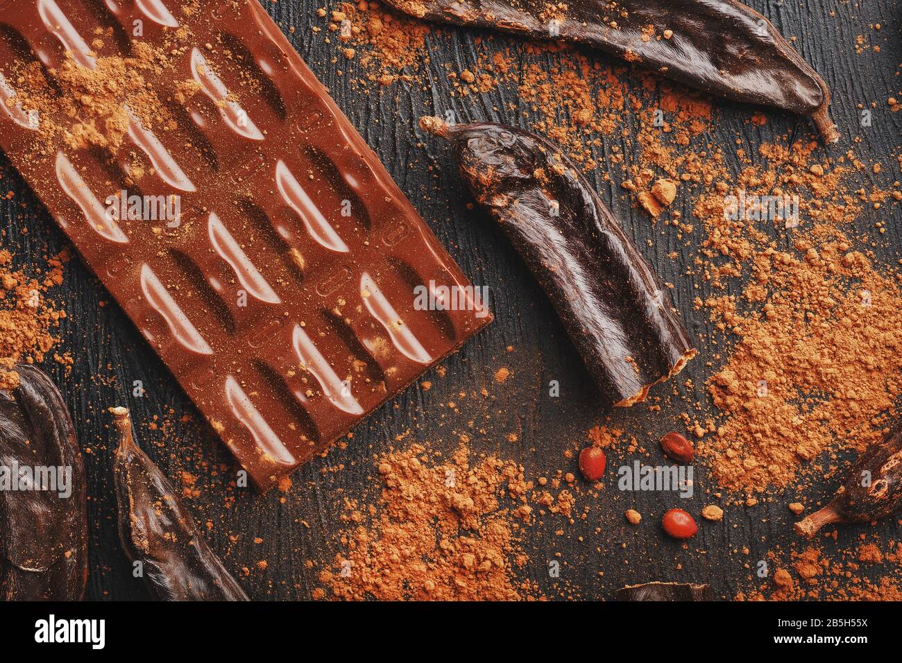 Carob chocolate and carob fruit powder on dark background. A tasty and