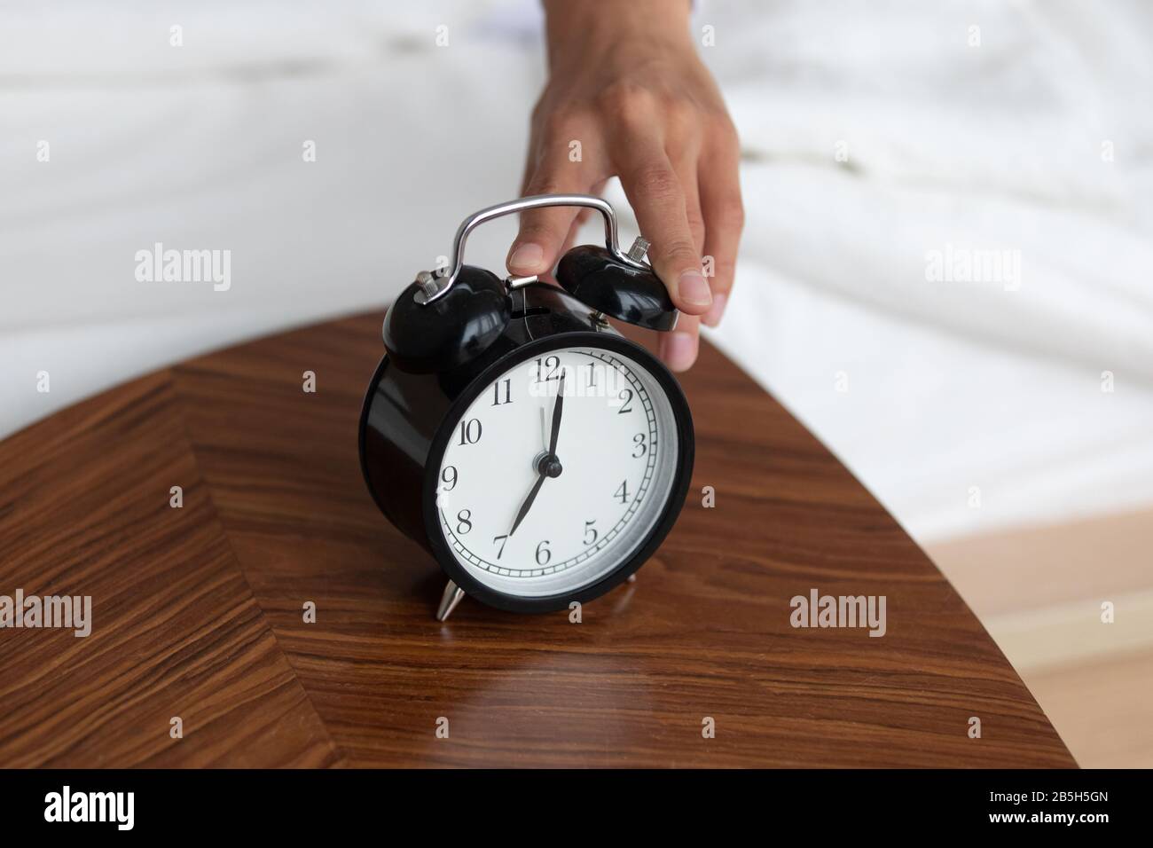 Female turn off wind-up alarm clock at home Stock Photo