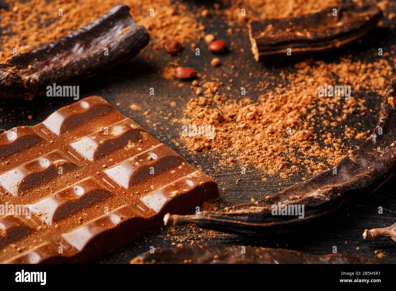 The pods of the carob chocolate bar on a black background. Sweets, chocolate and confectionery