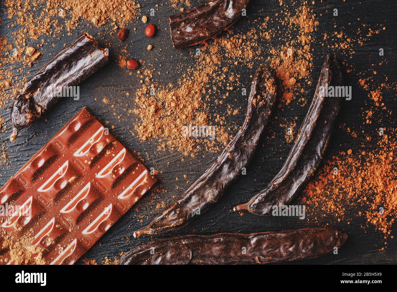 Carob chocolate and carob fruit powder on dark background. A tasty and useful substitute for