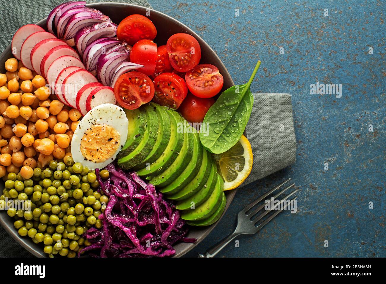 Healthy vegan lunch bowl. Avocado, chickpeas, tomato, red cabbage, green peas, red onion and radish vegetables salad. Healthy balanced vegetarian food Stock Photo