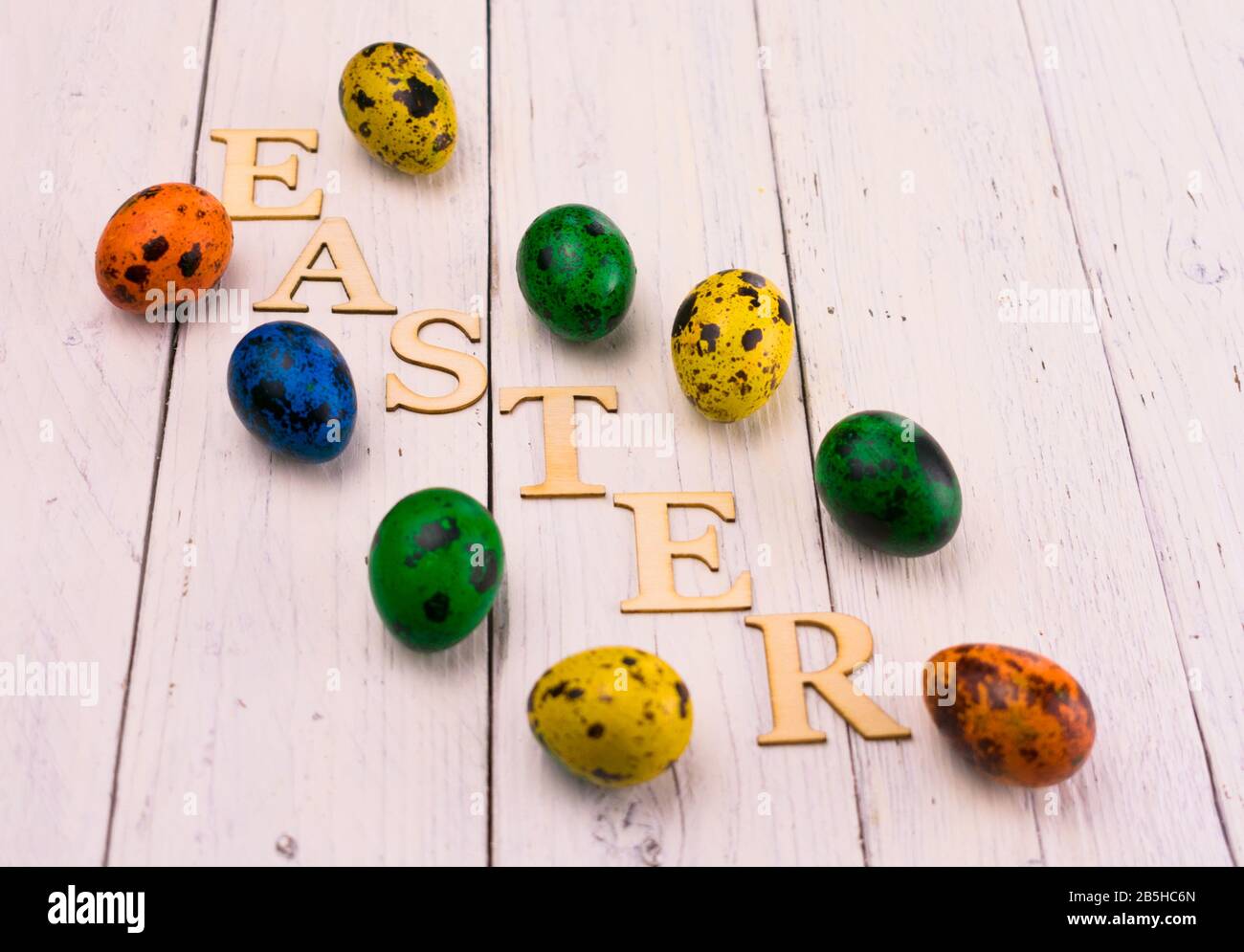 Multi-colored Easter quail eggs and the inscription Easter on a white wooden background. Stock Photo
