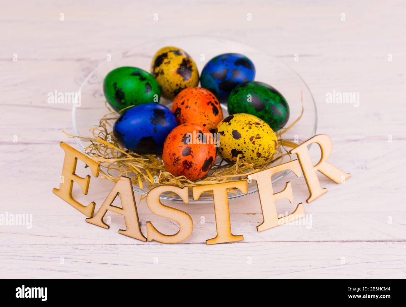 Multi-colored Easter quail eggs and the inscription Easter on a plate. Copy space. Stock Photo