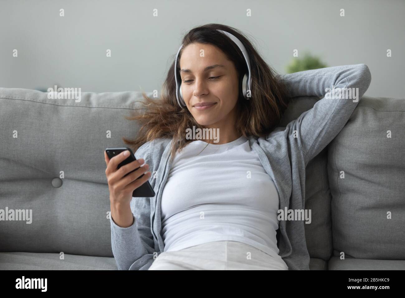 Millennial girl in headphones enjoy music on smartphone Stock Photo