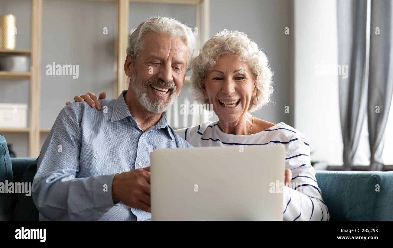 Overjoyed mature couple rest on sofa using laptop Stock Photo