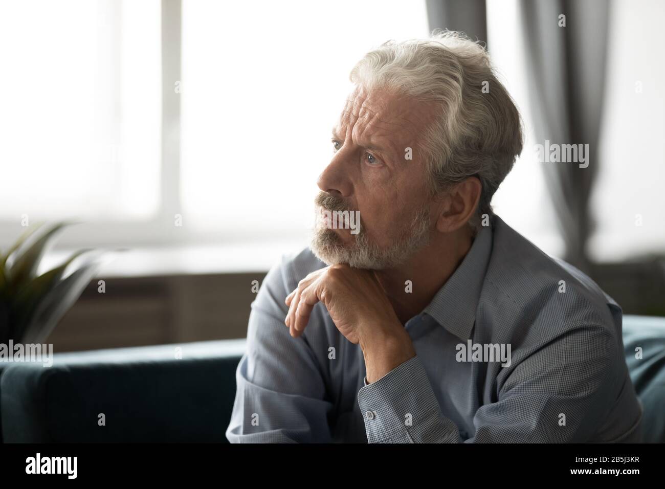 Depressed elderly man lost in thoughts mourning at home Stock Photo