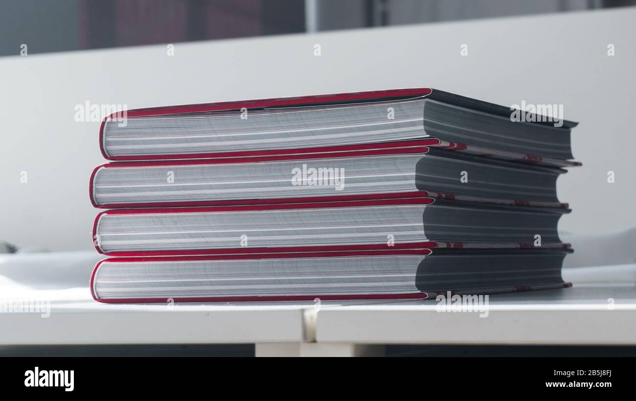 Stack of four thick new books on a white table Stock Photo