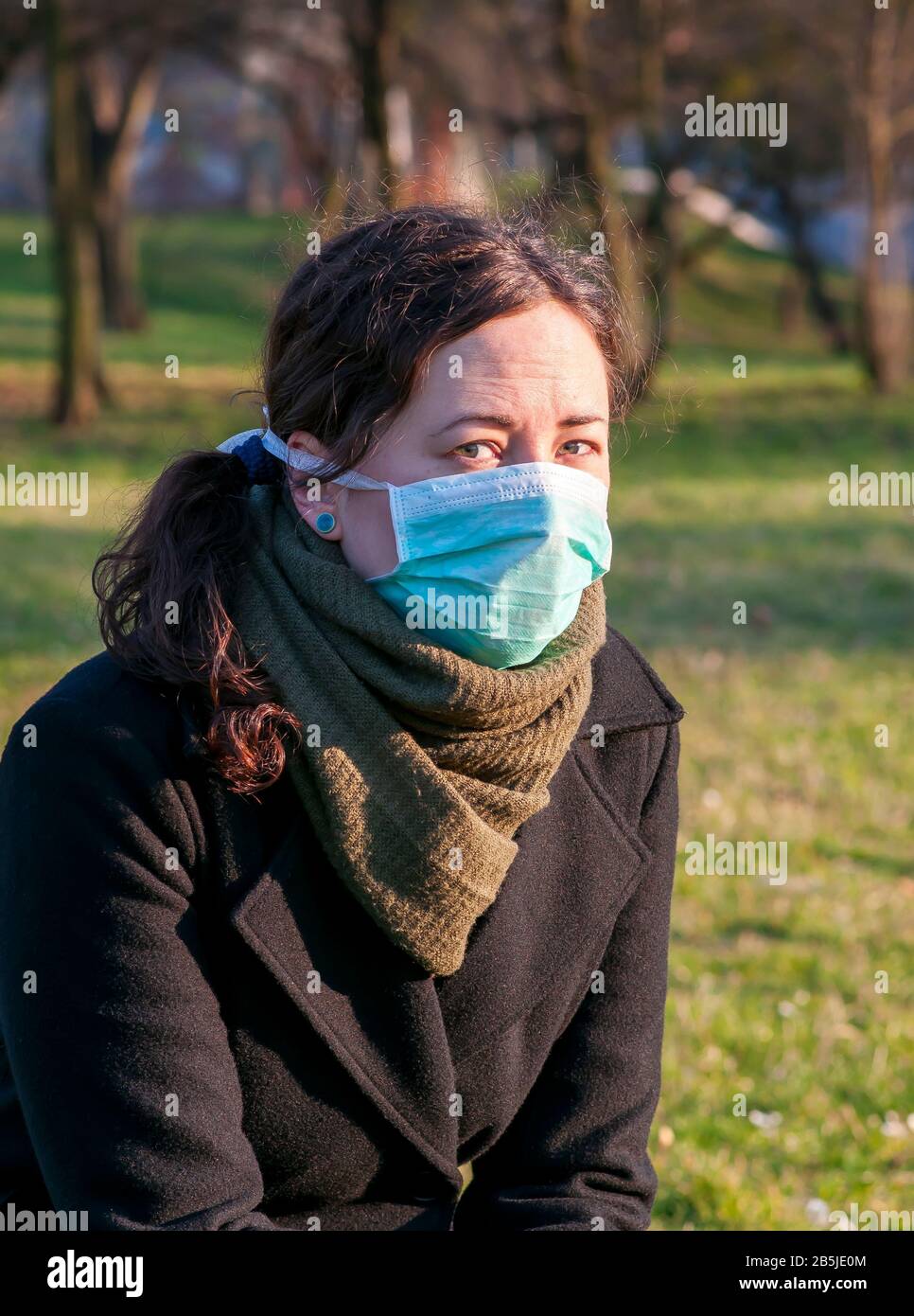 Portrait of a caucasian brunette woman in park in protective medical mask on face protection for spreading of disease virus SARS-CoV-2, Coronavirus, C Stock Photo