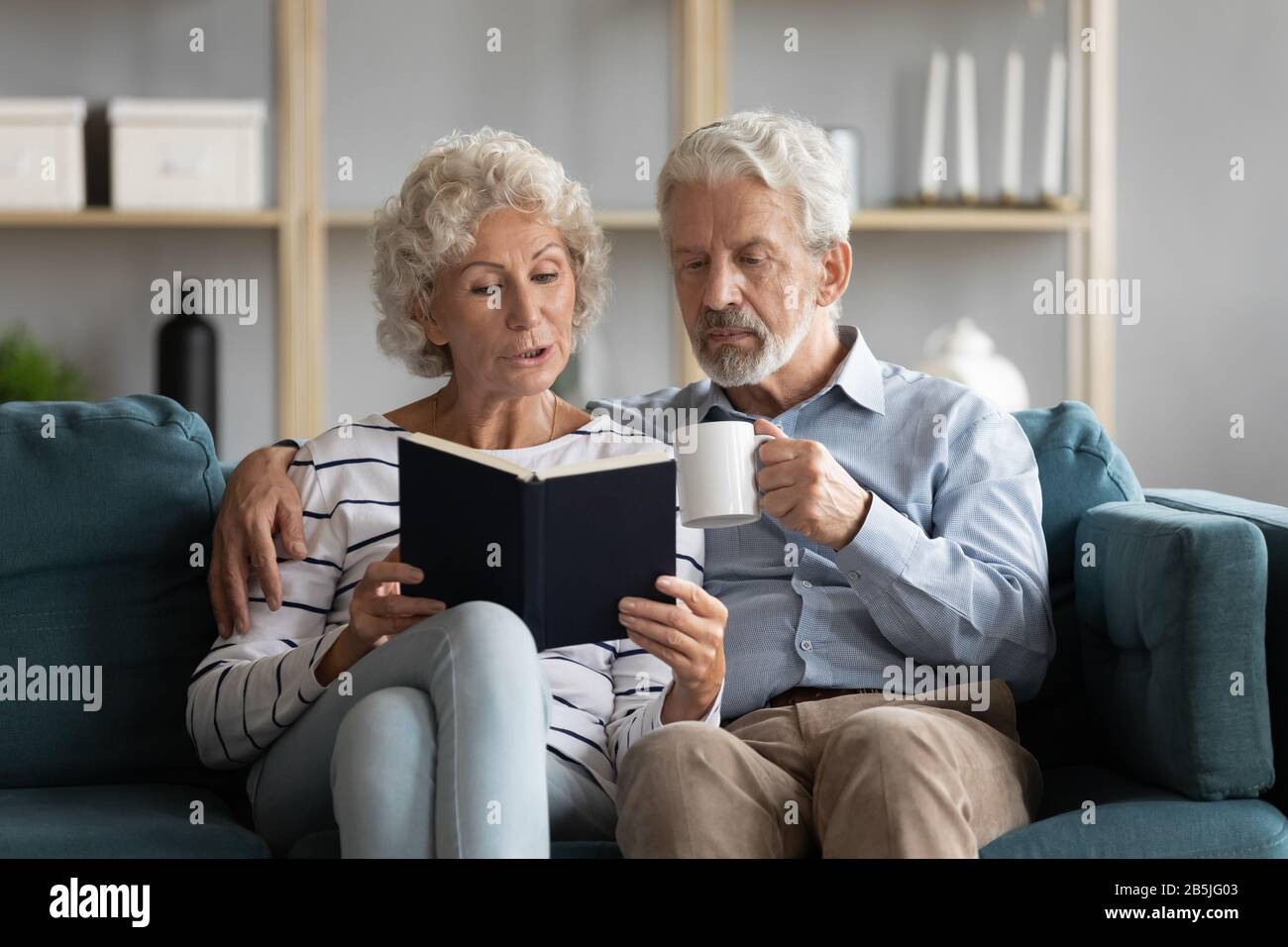 Elderly 60s couple relax on couch reading book together Stock Photo