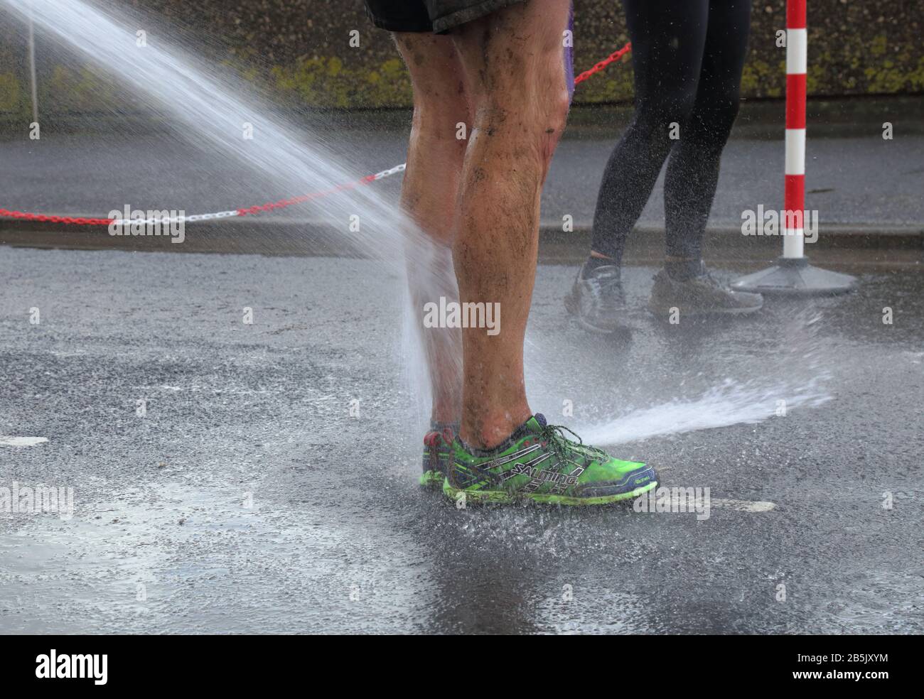 Washing shoes with water hose after finishing multi terrain 20 mile The Grizzly race in Seaton, Devon featuring 2000 runners Stock Photo
