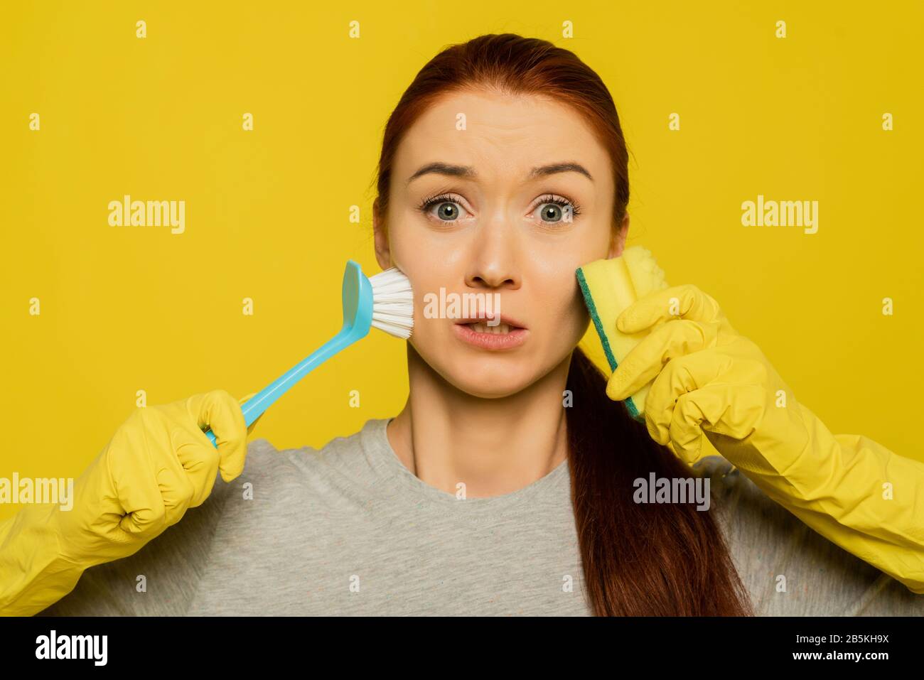 Lovely lovely woman holds a dishwashing brush and a sponge in yellow rubber gloves. The concept of skin cleansing, exfoliation of old skin and makeup remover. Beauty Face Skin Care. Stock Photo