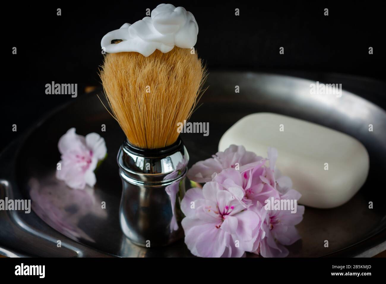 Shaving brush with foarm on top and geranium flowers of tender pink color  and white soap on the side on aged steel vase on black background. Skin care  Stock Photo - Alamy