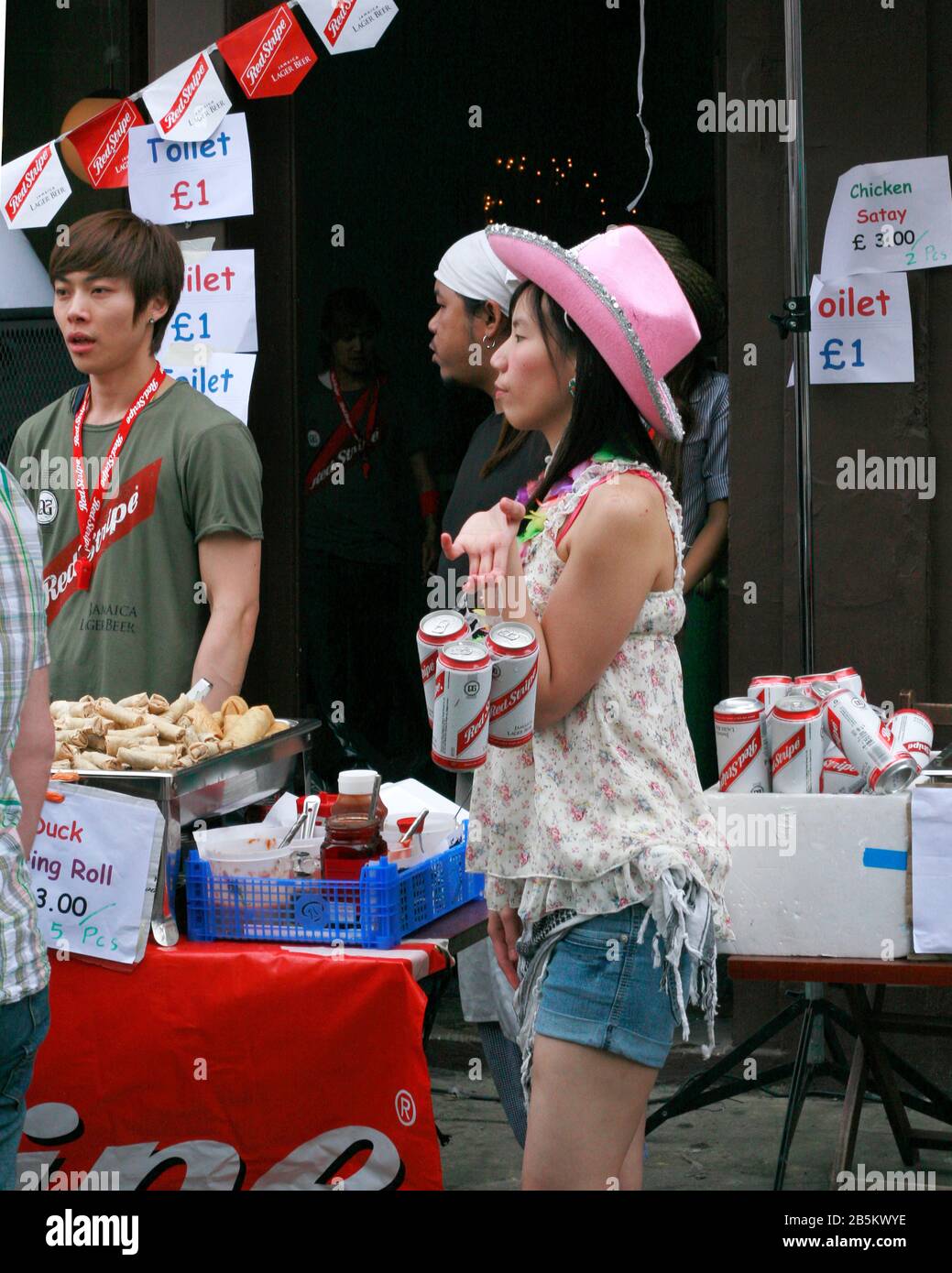 Asian lady in pink stetson selling red stripe beer at Notting Hill carnival, London Stock Photo