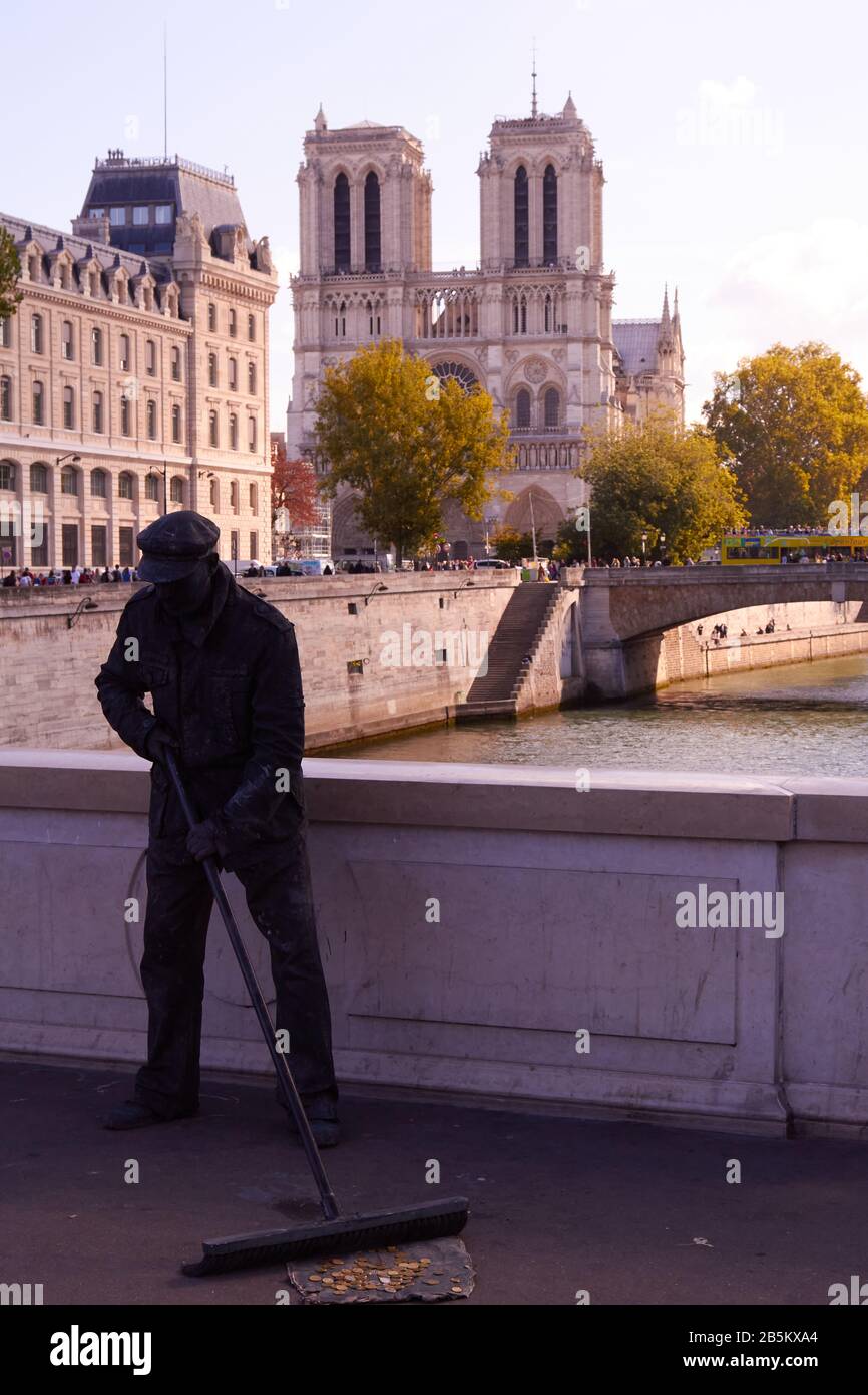 Live statue street artist sweeping on bridge with Notre Dame Cathedral in background, Paris Stock Photo