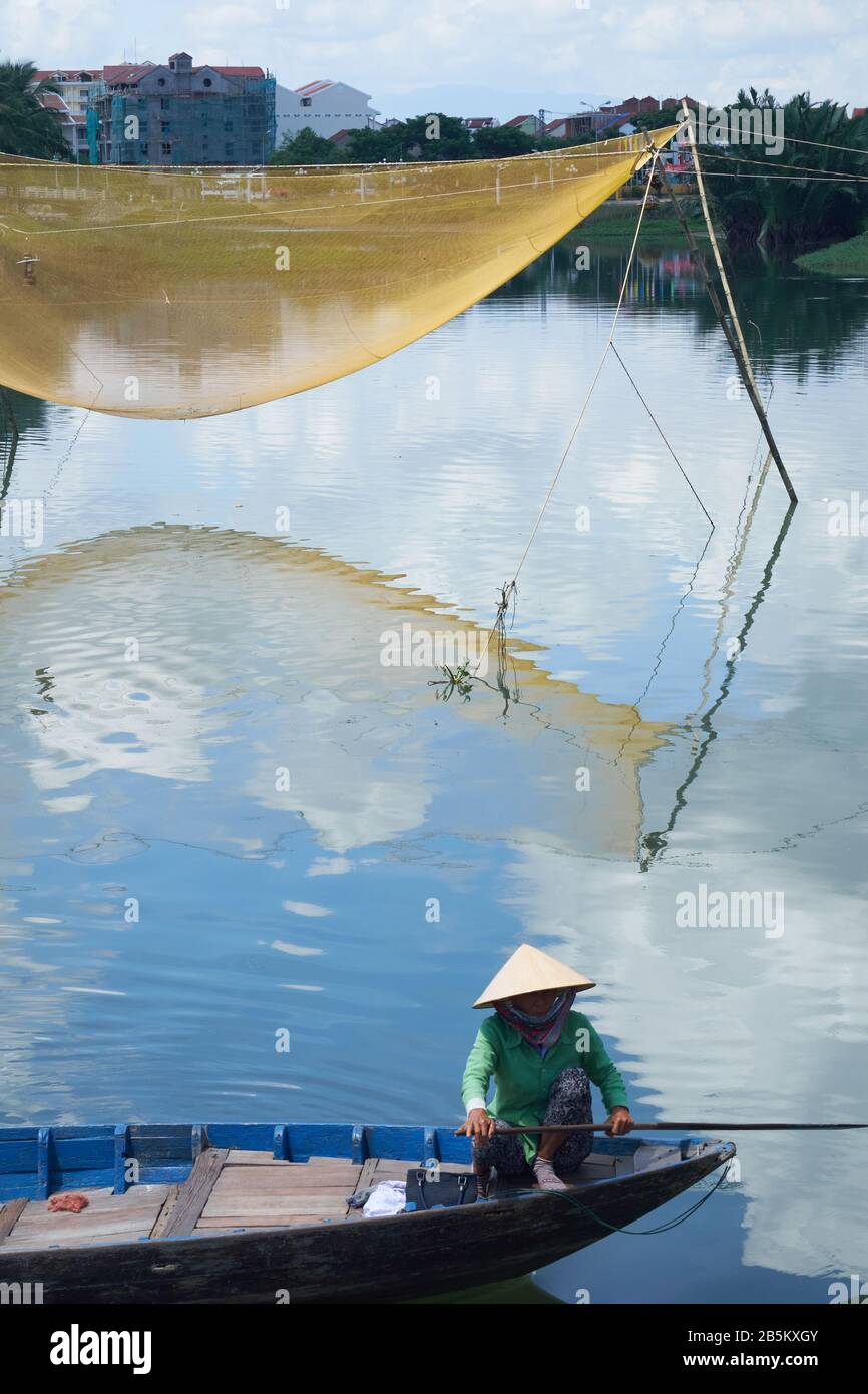 Elderly vietnamese woman rowing boat past fishing net in Hoi Ann Stock Photo